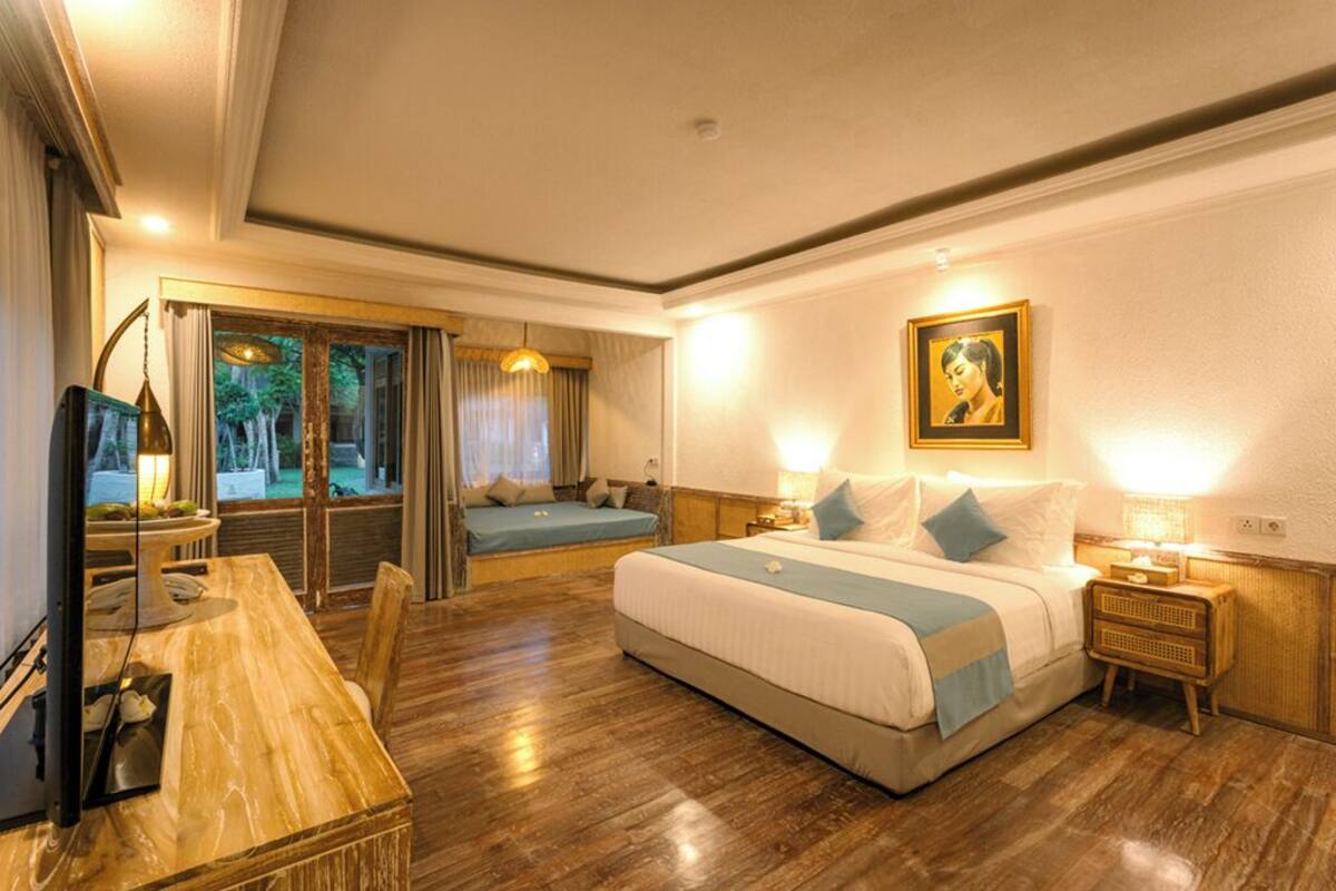 Habitación de hotel con una cama grande, un escritorio, una silla, un televisor y una ventana con vistas a árboles.