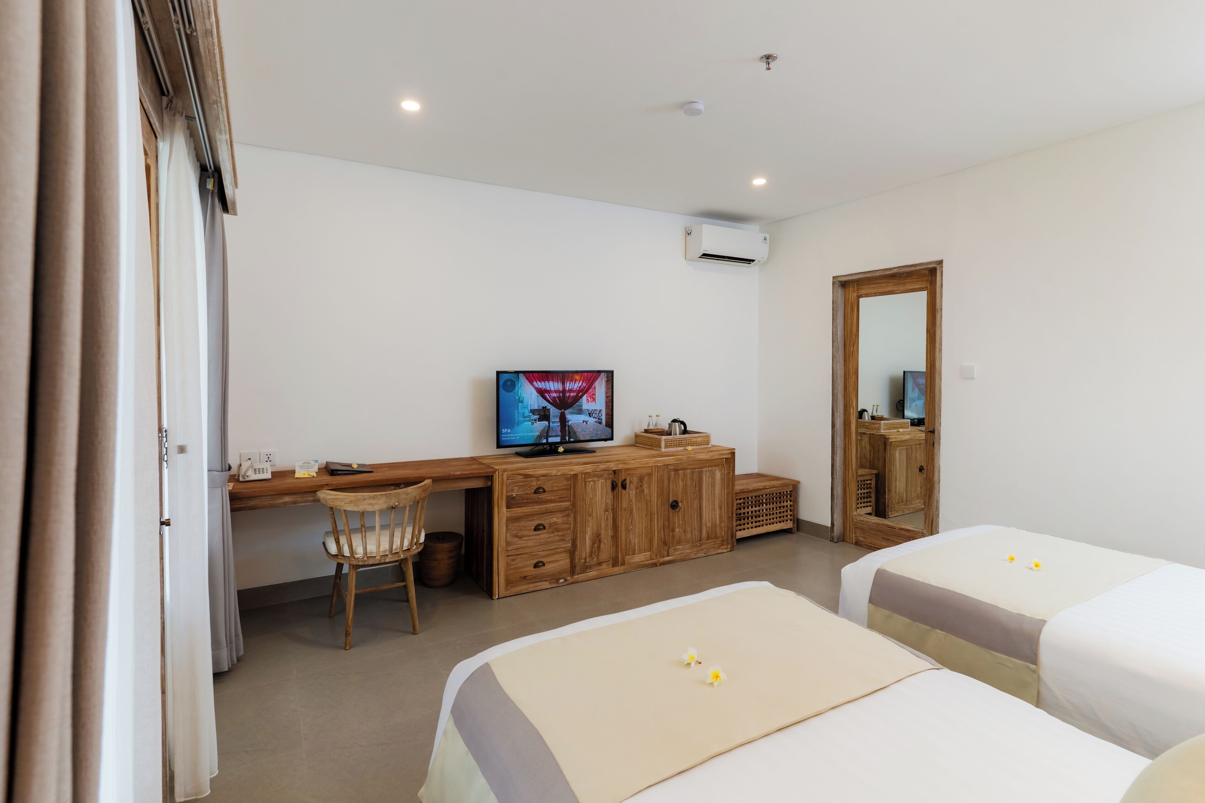 Une chambre d’hôtel avec un bureau en bois, une télévision, deux lits et un miroir.