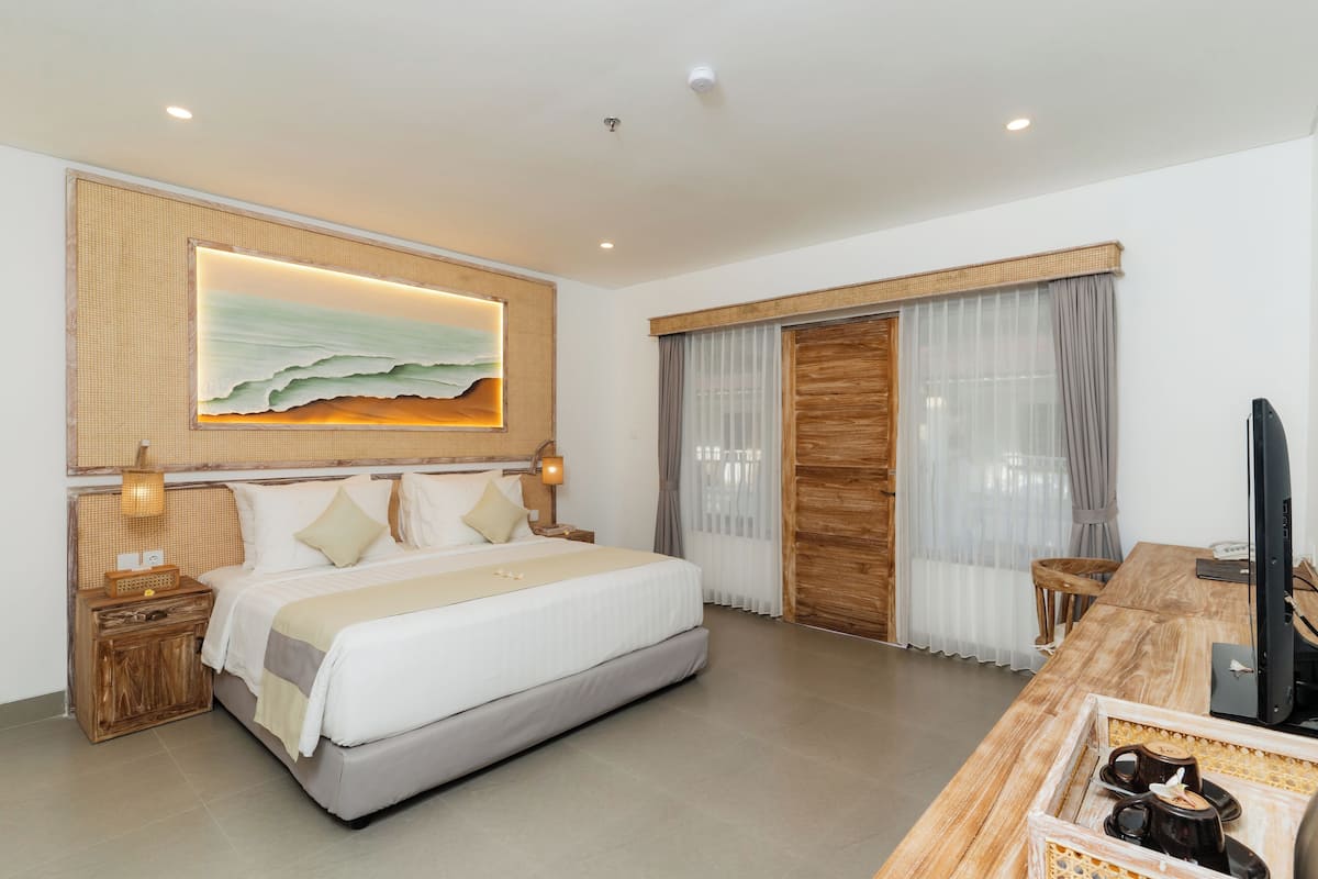 Una habitación de hotel moderna con una cama grande, un escritorio con computadora y un ventanal con cortinas.