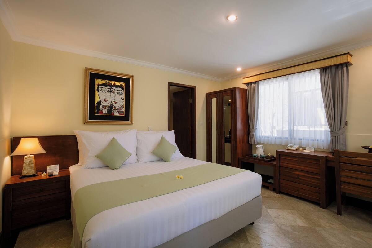 Una habitación de hotel con una cama grande, una mesita de noche con lámpara, un aparador y un espejo.