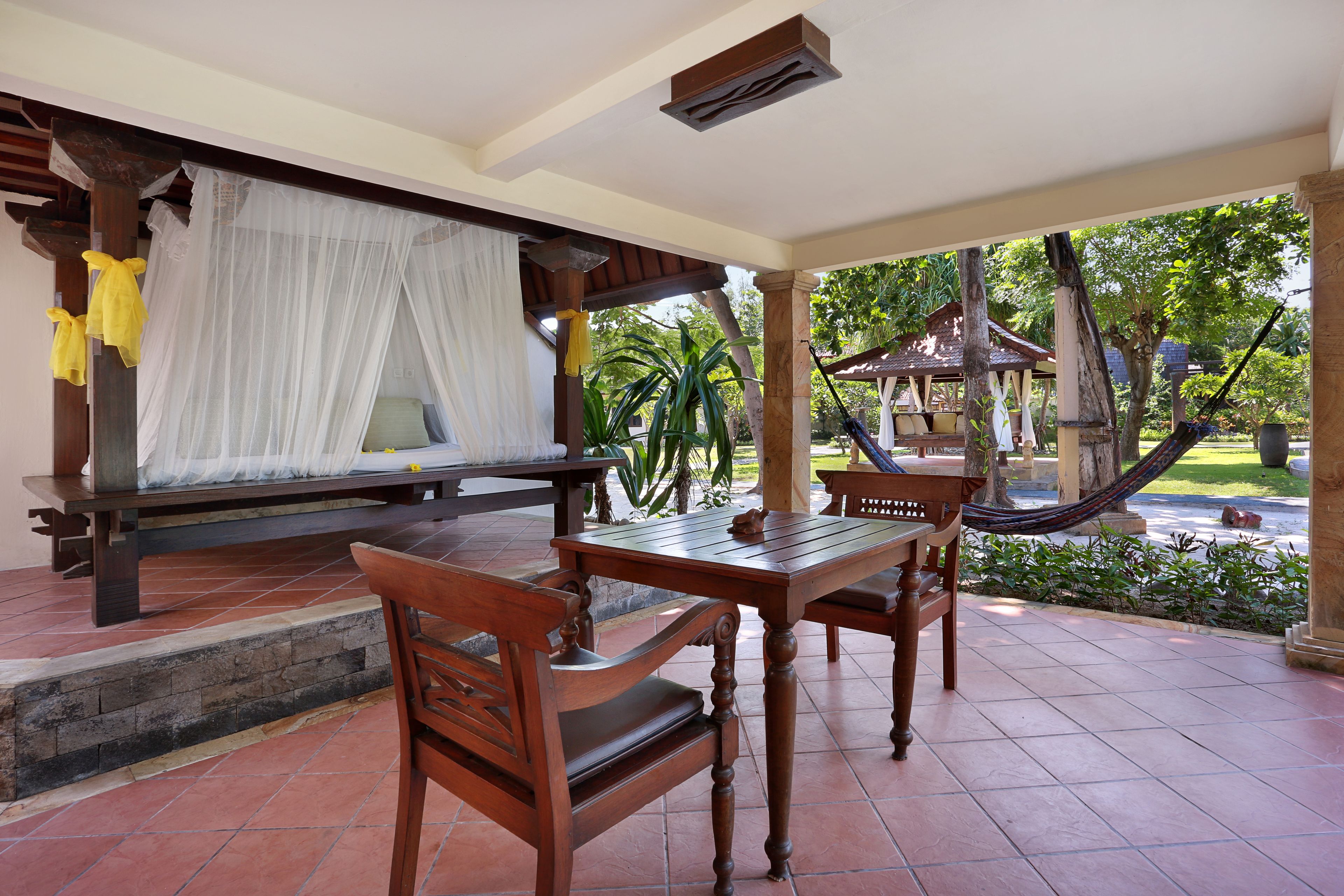 A wooden table and chairs set on a tiled patio with a white canopy and a hammock.