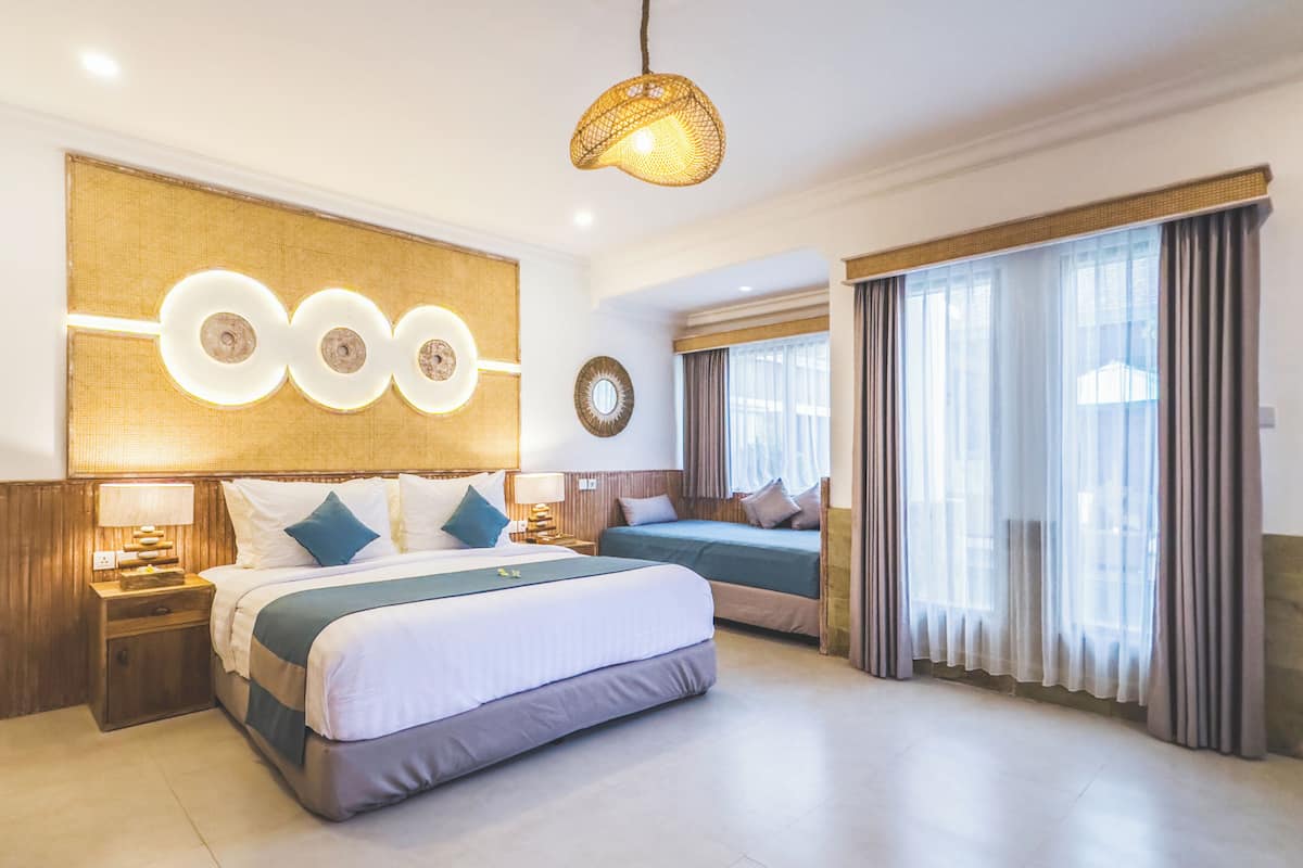 Una habitación de hotel con una cama grande, una cama más pequeña, un adorno de pared y un amplio ventanal con cortinas.