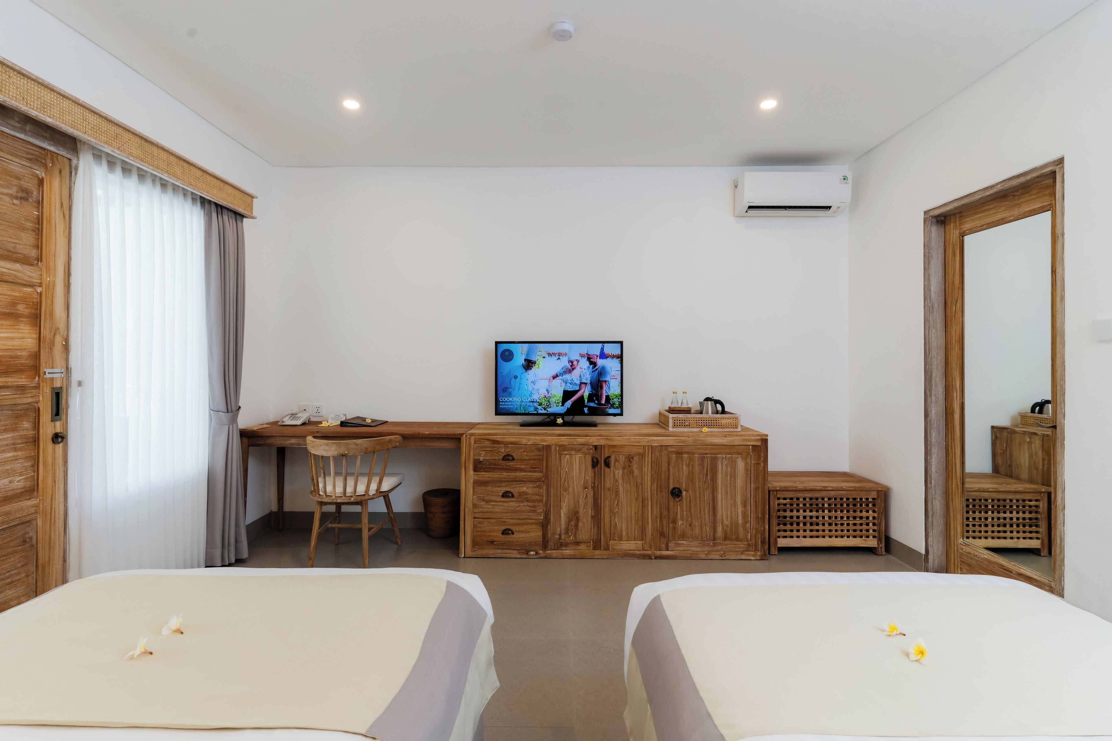 Una habitación de hotel con dos camas, un escritorio de madera, un televisor y un espejo grande.