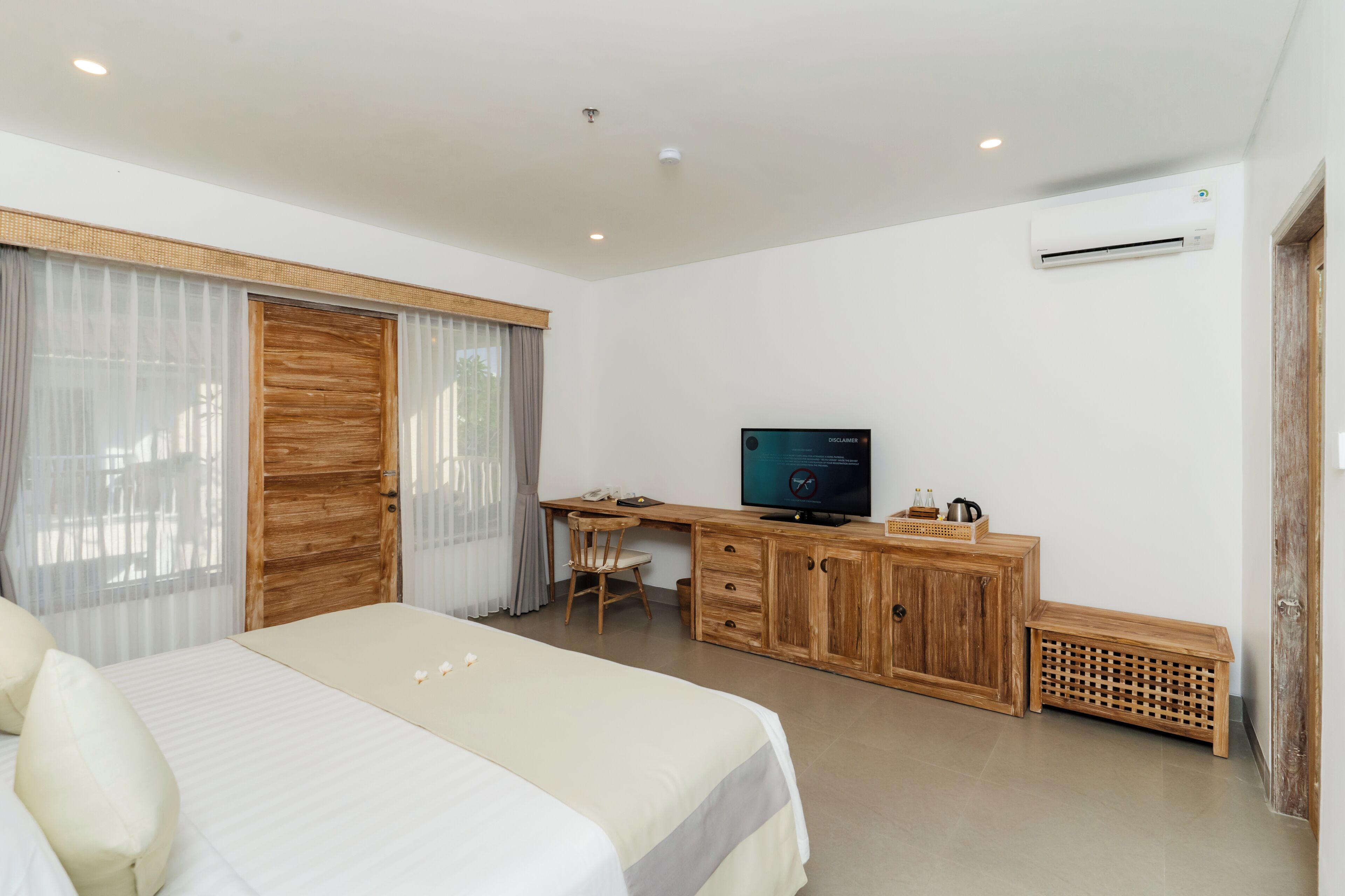 A hotel room with a bed, a desk, a television, and an air conditioning unit.