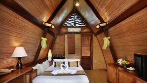 Een gezellige, driekantige kamer met een bed, nachtkastje, lamp en een televisie.