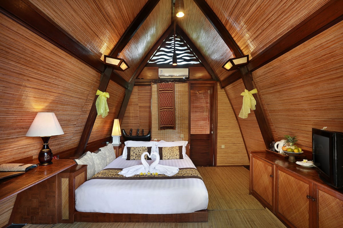Una habitación acogedora de forma triangular con cama, mesita de noche, lámpara y televisor.