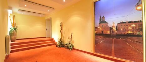 A hotel lobby with a view of a city square at dusk, featuring a staircase and a large window.