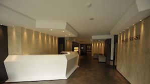 Un moderno vestíbulo de hotel con una recepción, una pared con la señalización 'PARCO SASSI' y un suelo de baldosas.