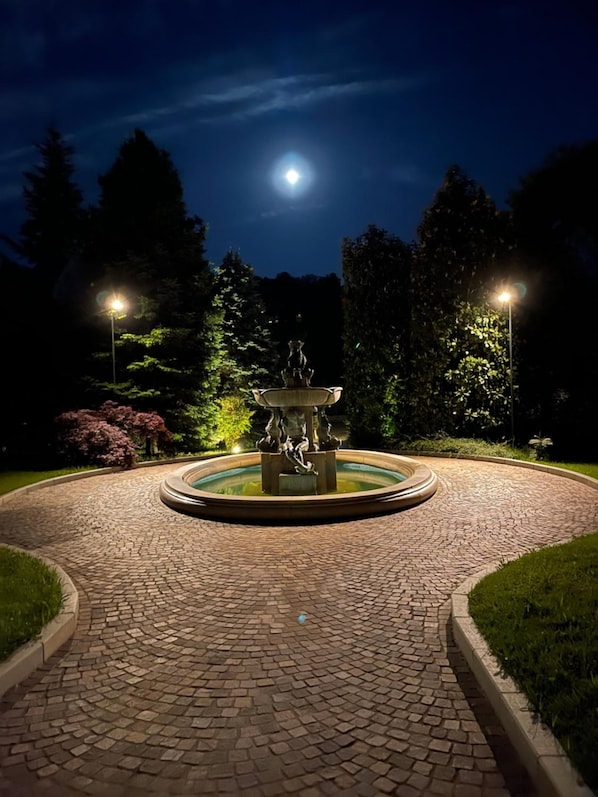 Un sendero circular de ladrillo que conduce a una fuente, con una luna de fondo.