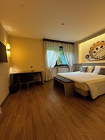 Una camera d'albergo moderna con pavimento in legno, un letto con testiera, una scrivania con sedia, una panca e una finestra con tende.