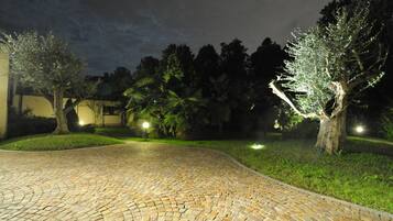 A paved pathway leading through a landscaped area with trees and a building in the background.