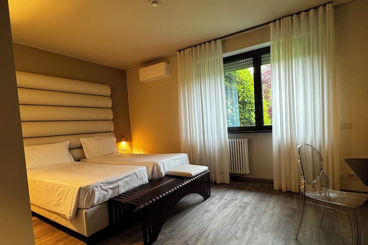 Un dormitorio moderno con una cama grande, un banco, una silla y una ventana con cortinas.