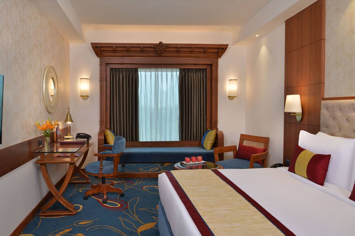 Una habitación de hotel con una cama grande, un escritorio con una silla, un sofá y una ventana con cortinas.