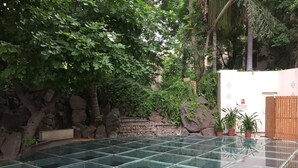A glass-tiled pool surrounded by greenery and a stone wall.