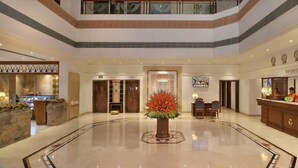 A hotel lobby with a reception desk, a large decorative plant, and a reception area with a clock.