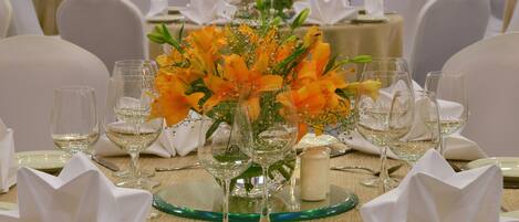 Una mesa de banquete dispuesta con servilletas blancas, cristalería transparente y flores naranjas.