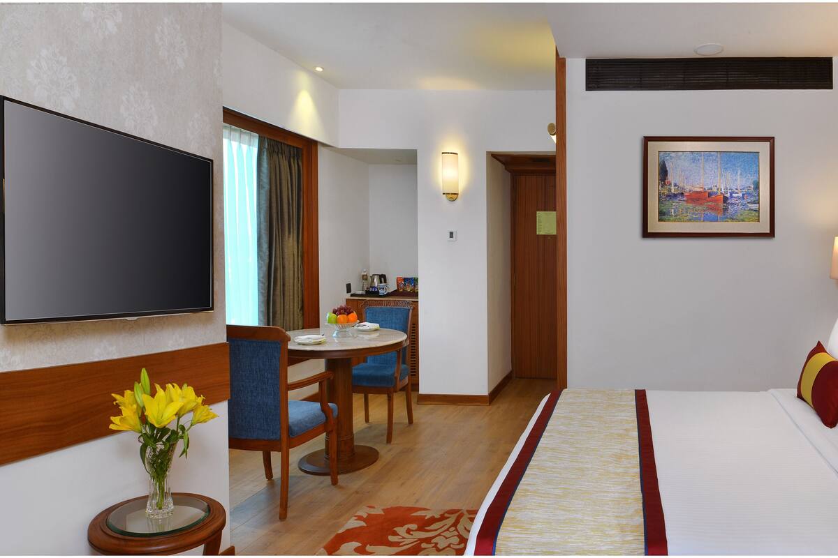 Una habitación de hotel con cama, televisor, zona de comedor con sillas y mesa, y un cuadro en la pared.