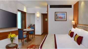 A hotel room with a bed, a TV, a dining area with chairs and a table, and a painting on the wall.