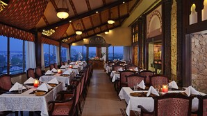 A restaurant with tables set for dining, large windows offering city views, and ornate architectural details.
