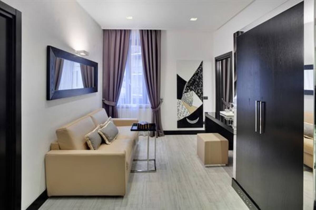A modern hotel room with a beige sofa, a large black refrigerator, and a minimalist decor.