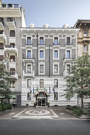 A historic hotel facade with a symmetrical design, multiple balconies, and a central entrance with flags.