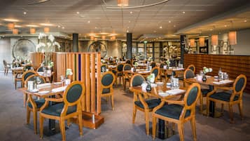 Un restaurante espacioso con mesas y sillas de madera, un separador decorativo central e iluminación colgante.