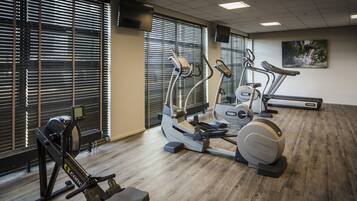 A gym with cardio machines, large windows with blinds, and a painting on the wall.