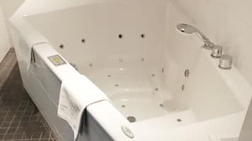 Eine große, rechteckige Badewanne mit mehreren Düsen, einer Handbrause und einer Bedienkonsole.