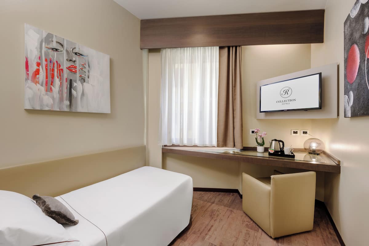 A hotel room with a bed, a desk, a chair, a TV, and artwork on the walls.