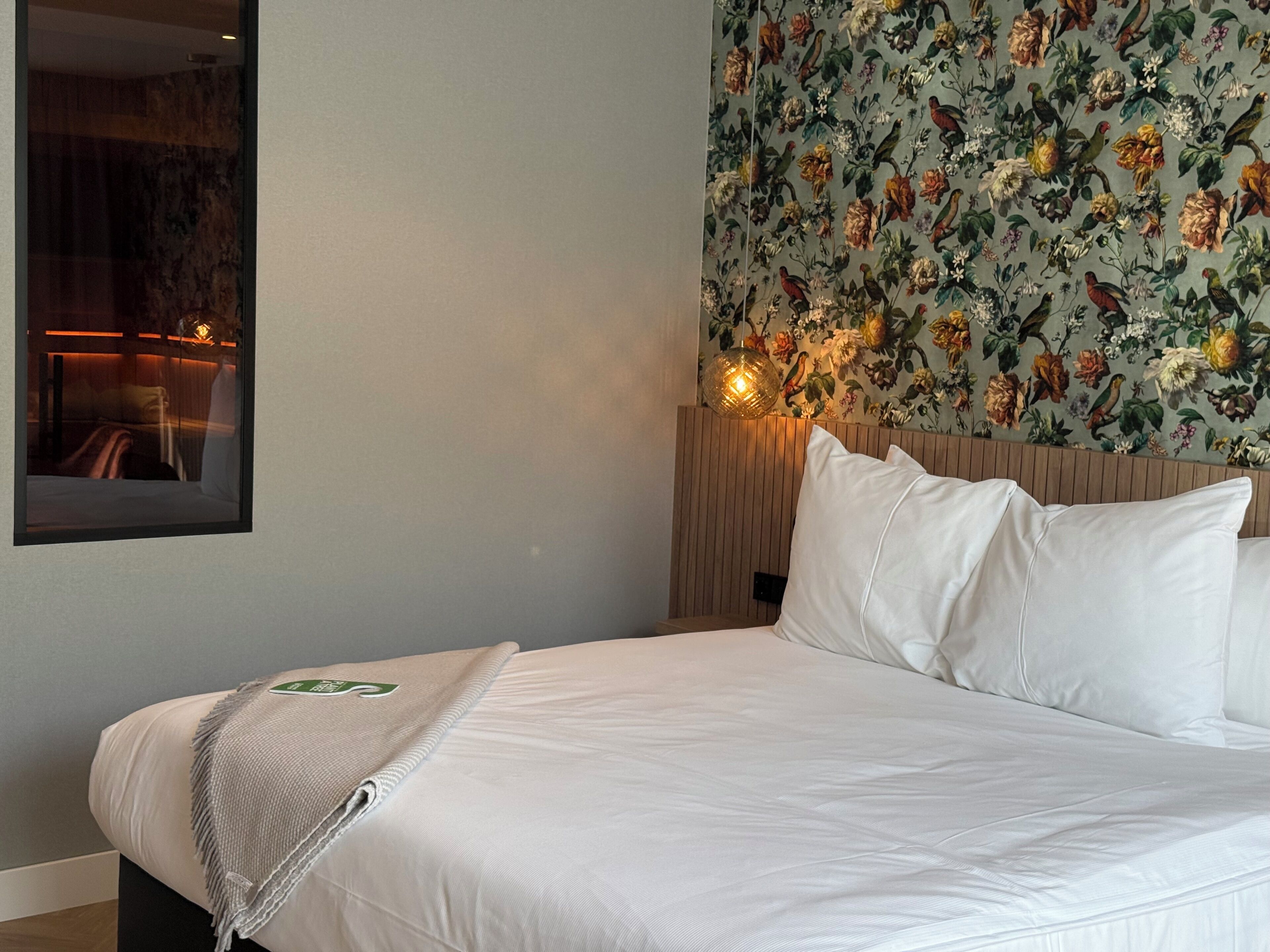 A hotel room with a bed, a mirror, and a floral wallpaper.