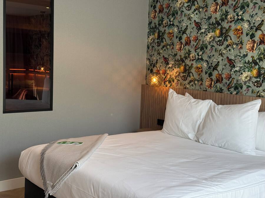 Una habitación de hotel con una cama, un espejo y papel tapiz floral.