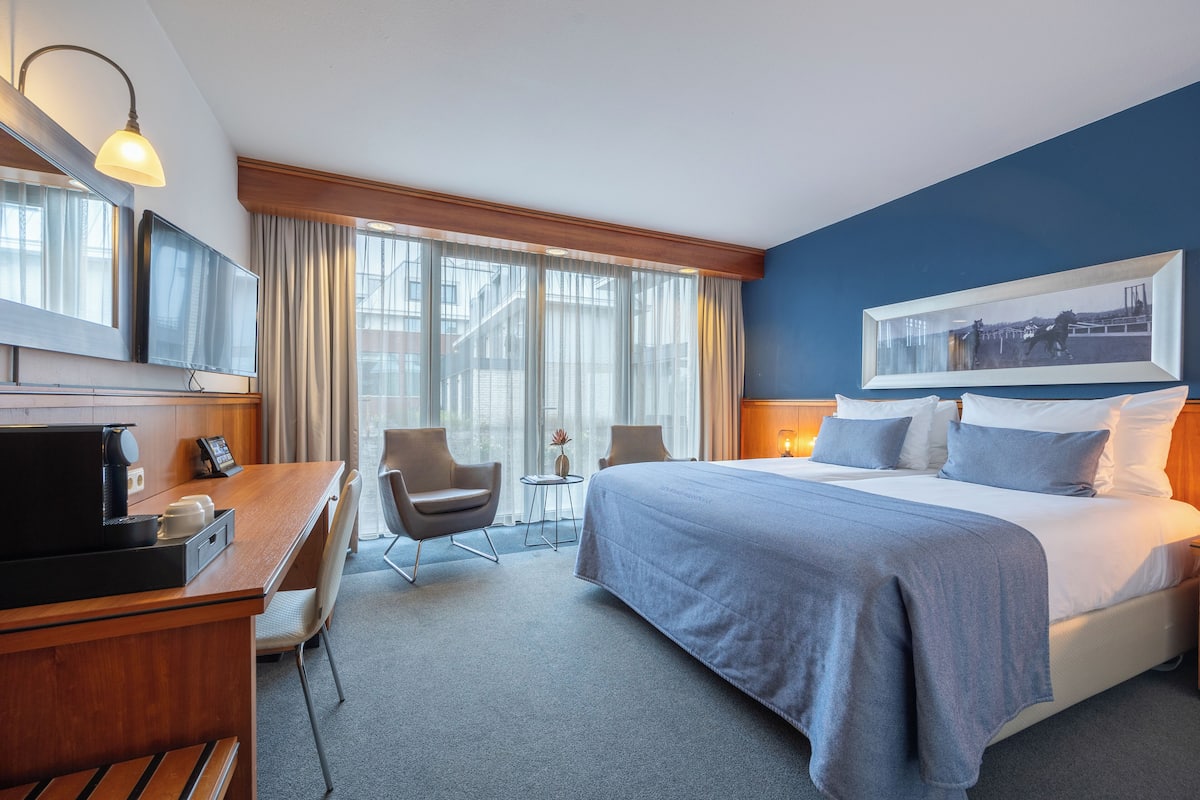 Ein Hotelzimmer mit Bett, Schreibtisch, Stuhl, Fernseher und einem Fenster mit Vorhängen.