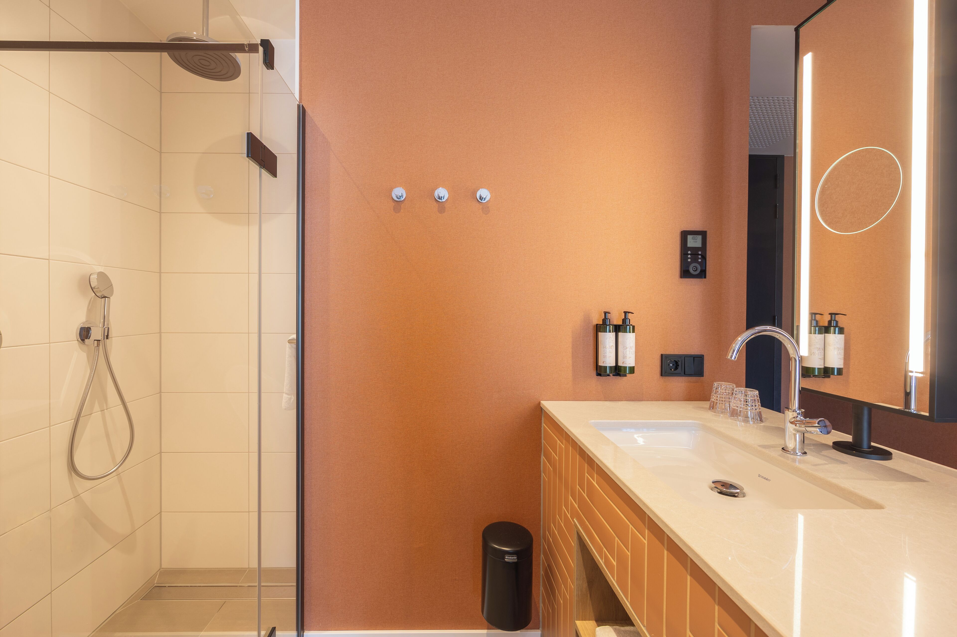 Een moderne badkamer met een douchecabine van glas, een wastafel met dubbele wastafel en een grote spiegel.