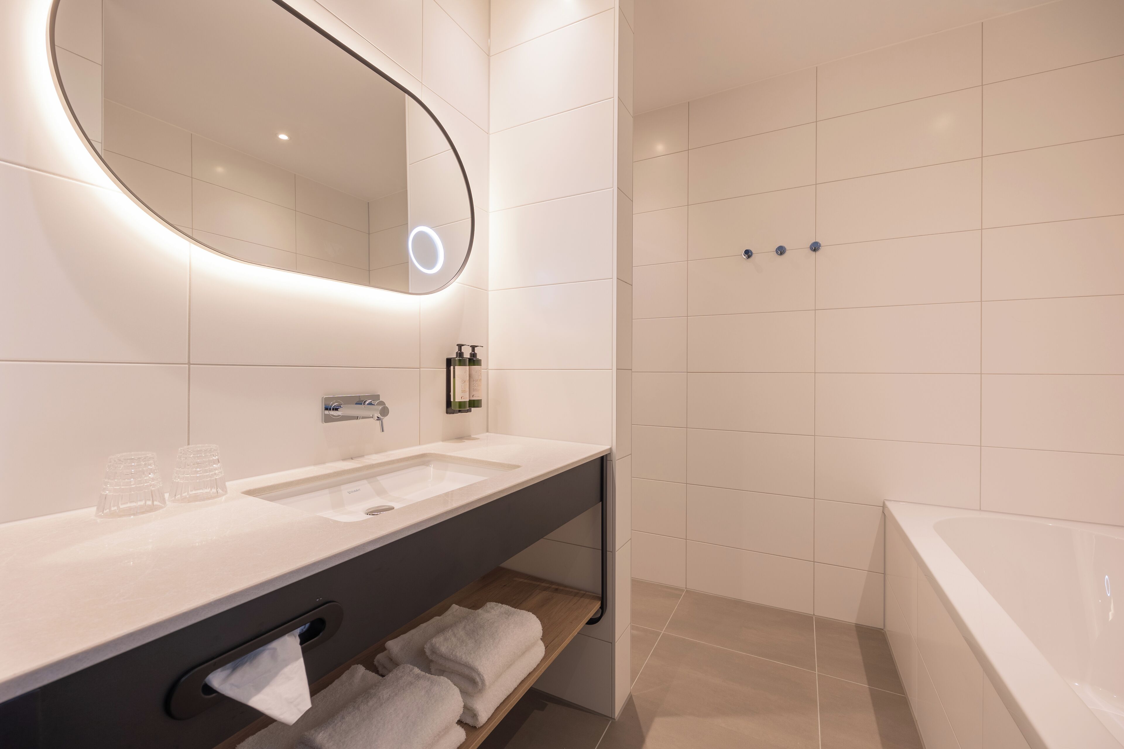 A modern bathroom with a large mirror, two sinks, a shower, and a bathtub.