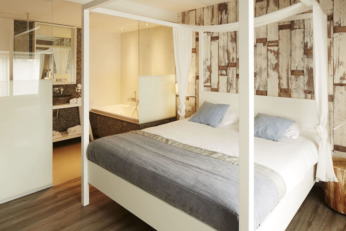 Ein modernes Schlafzimmer mit Baldachinbett, einem separaten Badezimmer mit Badewanne und einer Wand mit Holzvertäfelung.