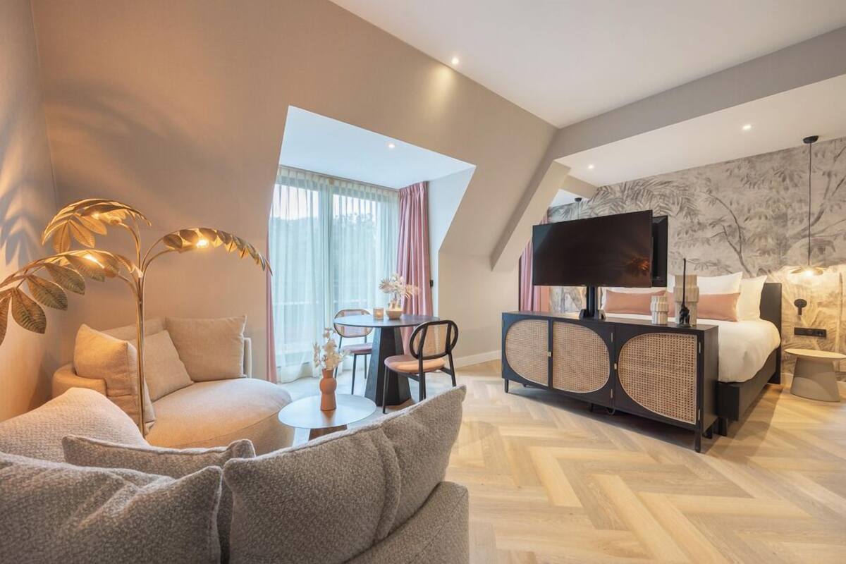 Ein modernes Hotelzimmer mit Sofa, Esstisch, Fernseher und Bett.