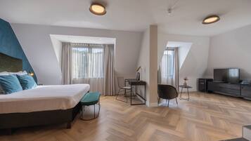 A modern hotel room with a bed, a desk, a chair, a TV, and a small table with a vase.