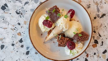 A bowl of dessert with ice cream, raspberries, and chocolate pieces on a speckled countertop.
