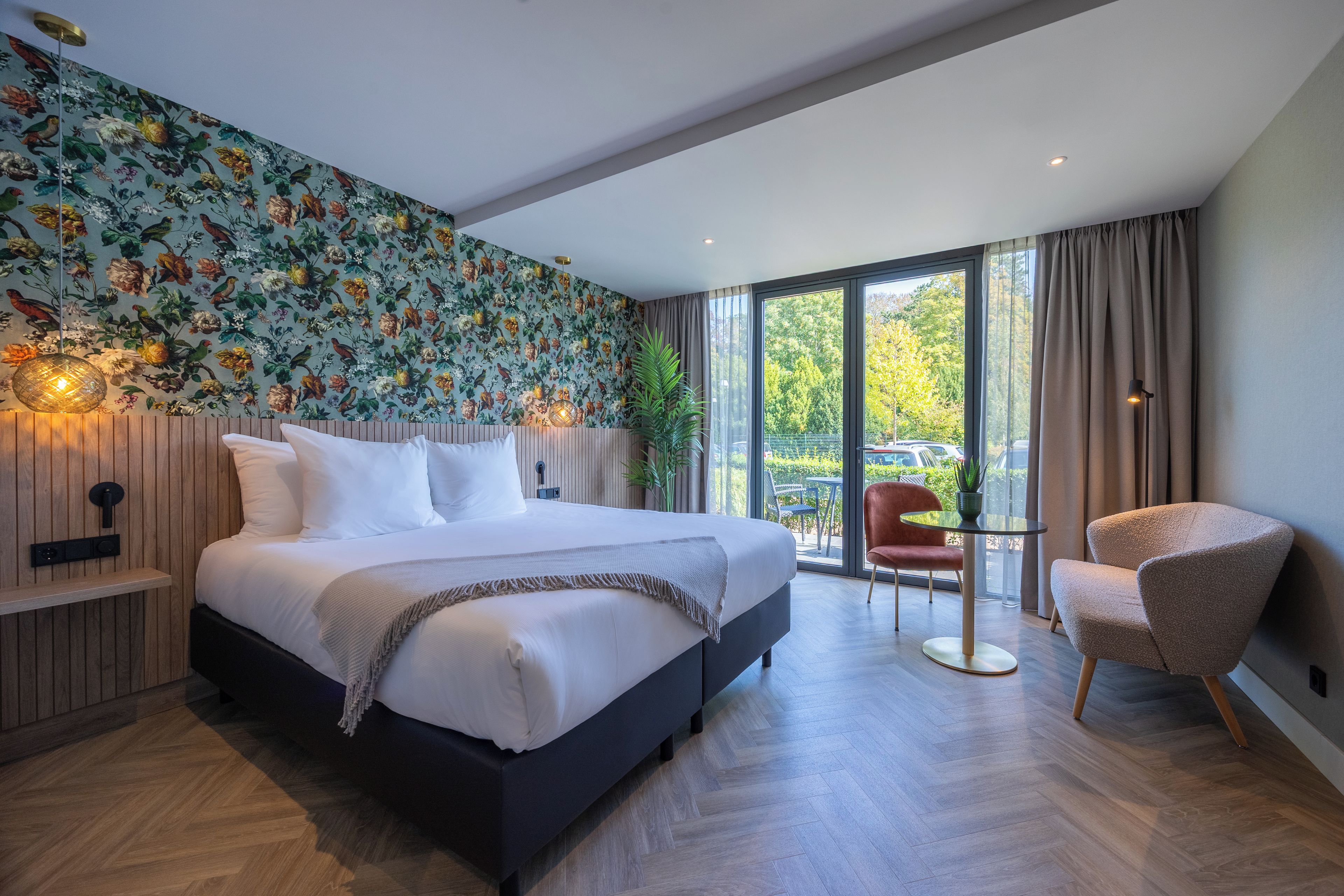 Ein modernes Schlafzimmer mit einem großen Bett, einem kleinen Tisch, einem Sessel und einem Balkon mit Aussicht.