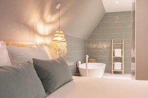 Quarto moderno com uma cama grande, abajur, banheira e escada de madeira.