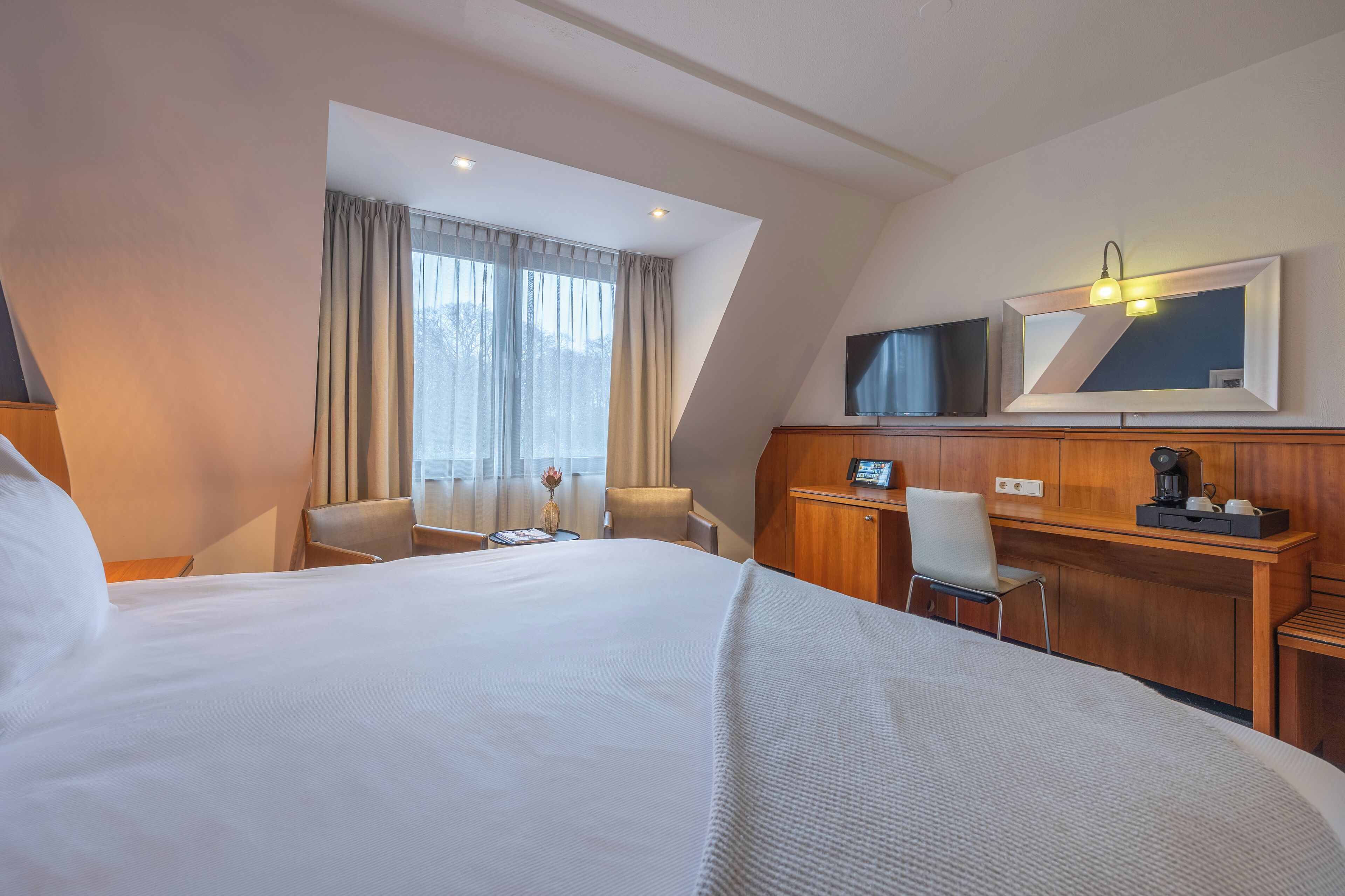 A hotel room with a large bed, a desk, a chair, a TV, and a window with curtains.