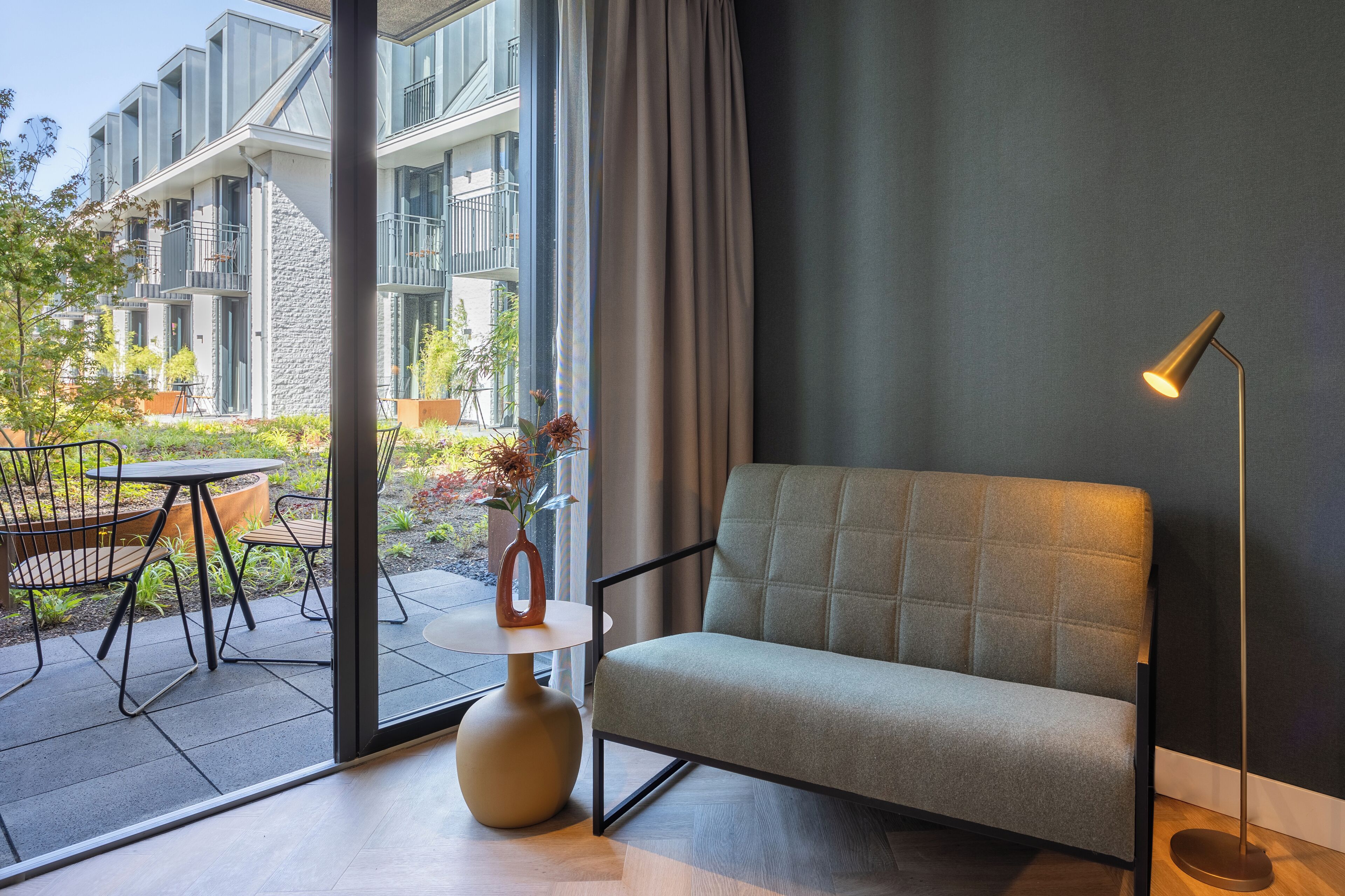 Een moderne woonkamer met een bank, een vloerlamp en een bijzettafeltje met een vaas.