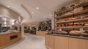 Un espace moderne dédié au petit-déjeuner, avec des comptoirs en bois, une variété de pains et une cuisine en arrière-plan.