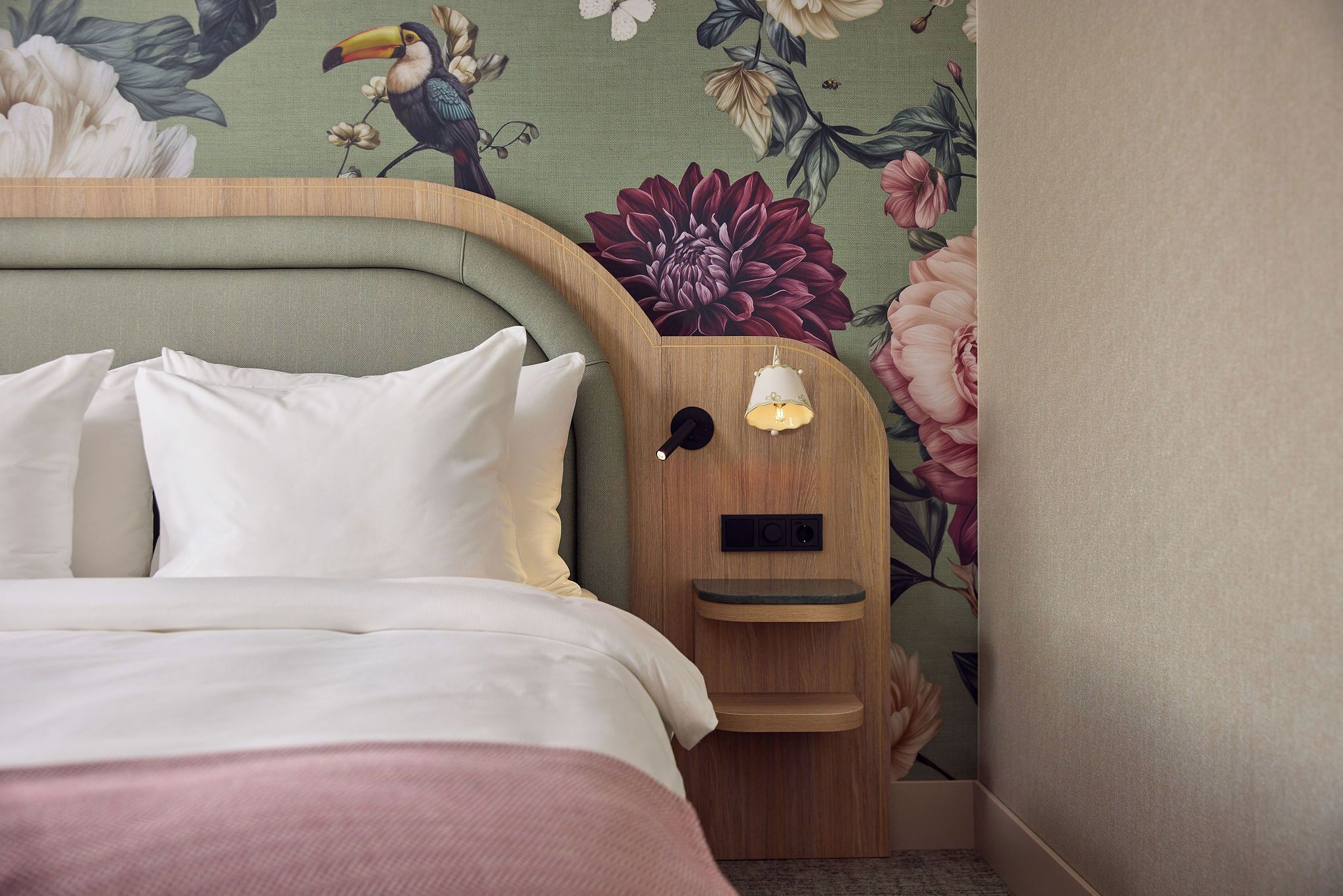 A hotel room with a bed, a nightstand, a lamp, and floral wallpaper.