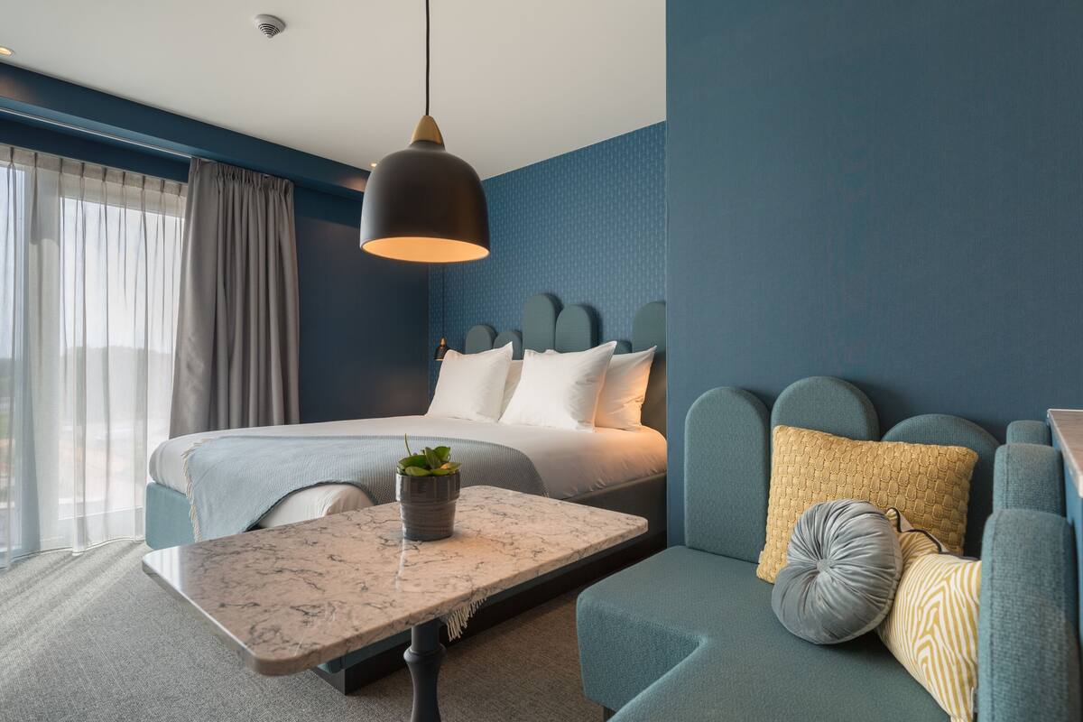 Une chambre d’hôtel moderne équipée d’un lit, d’un canapé, d’une table en marbre et d’un luminaire suspendu.