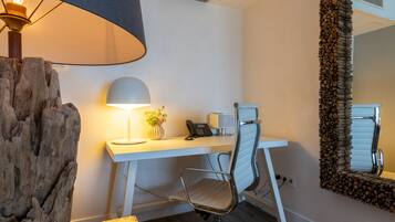 A modern office space with a white desk, a metal office chair, a lamp, a phone, and a decorative mirror.