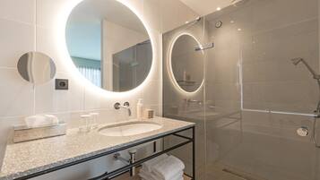 A modern bathroom with a large oval mirror, a sink, and a glass-enclosed shower.