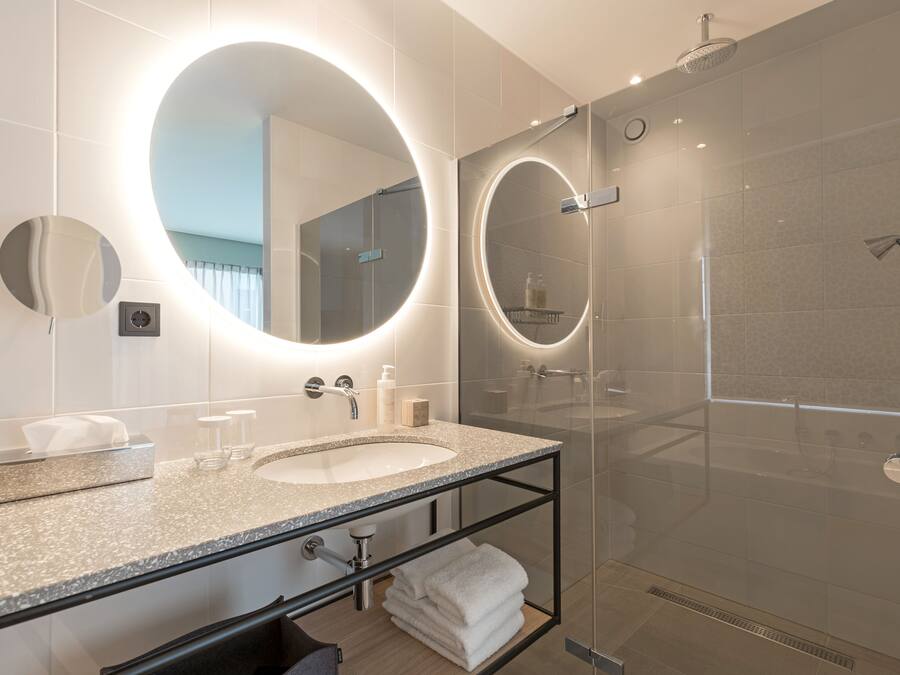 A modern bathroom with a large oval mirror, a sink, and a glass-enclosed shower.