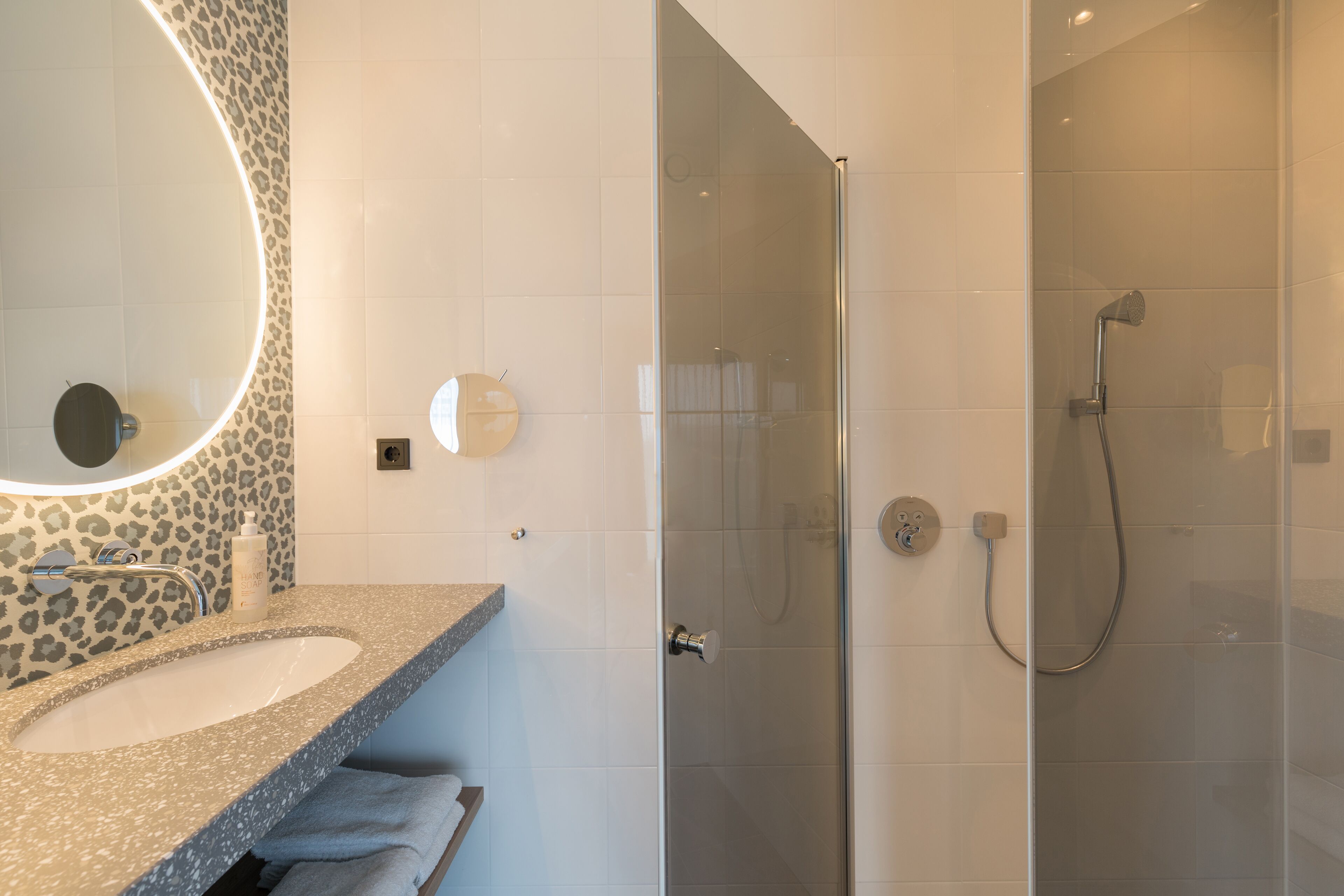 Un bagno moderno con lavabo su piano in granito, uno specchio rotondo e una cabina doccia in vetro.