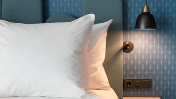 A bedroom with a bed, pillows, a bedside table, a lamp, and a wall with a patterned wallpaper.